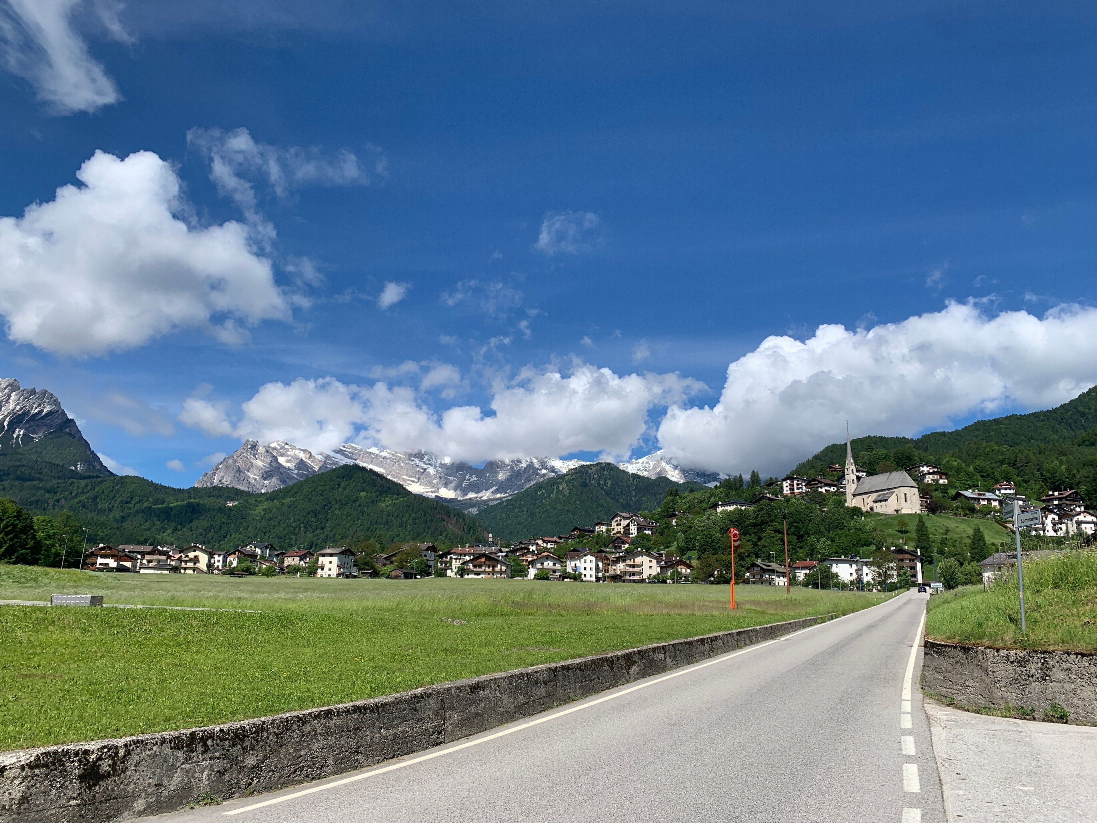 Une route menant à un village avec des maisons et une église, le tout entouré de montagnes.