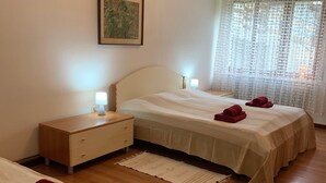 A hotel room with two beds, a nightstand, a bedside table, a lamp, a framed picture on the wall, and a window with sheer curtains. - Apartment 'Bruna' with Mountain View, Private Terrace and Wi-Fi (Forno di Zoldo)