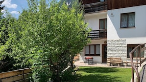 A building with a wooden balcony, a stone wall, and a grassy yard. - Apartment 'Bruna' with Mountain View, Private Terrace and Wi-Fi (Forno di Zoldo)