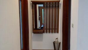 A hallway with a wooden door on the left, a window with vertical blinds, and a trash bin on the right. - Apartment 'Bruna' with Mountain View, Private Terrace and Wi-Fi (Forno di Zoldo)