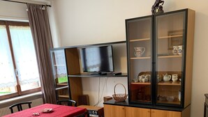 A living room with a dining table, chairs, a sofa, a television, and a cabinet with glass doors. - Apartment 'Bruna' with Mountain View, Private Terrace and Wi-Fi (Forno di Zoldo)