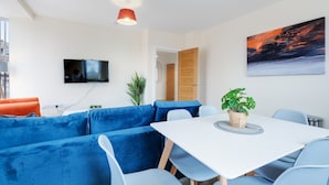 Una sala moderna con un sofá seccional, una mesa de comedor y un televisor de pantalla plana montado en la pared.