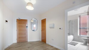 Un pasillo con suelo de madera, un espejo y una puerta que da a un baño con ducha, inodoro y ventana.