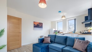 Una sala de estar moderna con un sofá seccional azul, una puerta de madera y una cocina al fondo.
