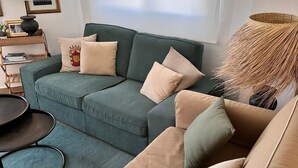 Ein Wohnzimmer mit einem grünen Sofa, beigen Kissen, einem runden Couchtisch und einer Lampe.