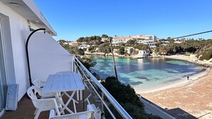 Ein Balkon mit Tisch und Stühlen, mit Blick auf einen Strand und ein Gewässer.