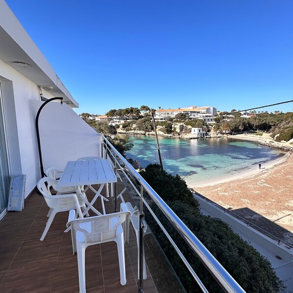A balcony with a table and chairs, overlooking a beach and a body of water.