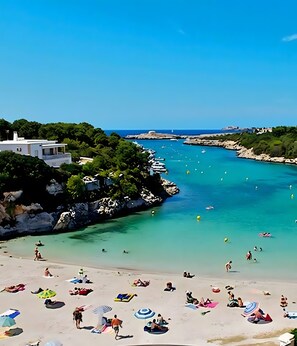 A beach with clear turquoise waters, rocky coastline, and a white building with a balcony.