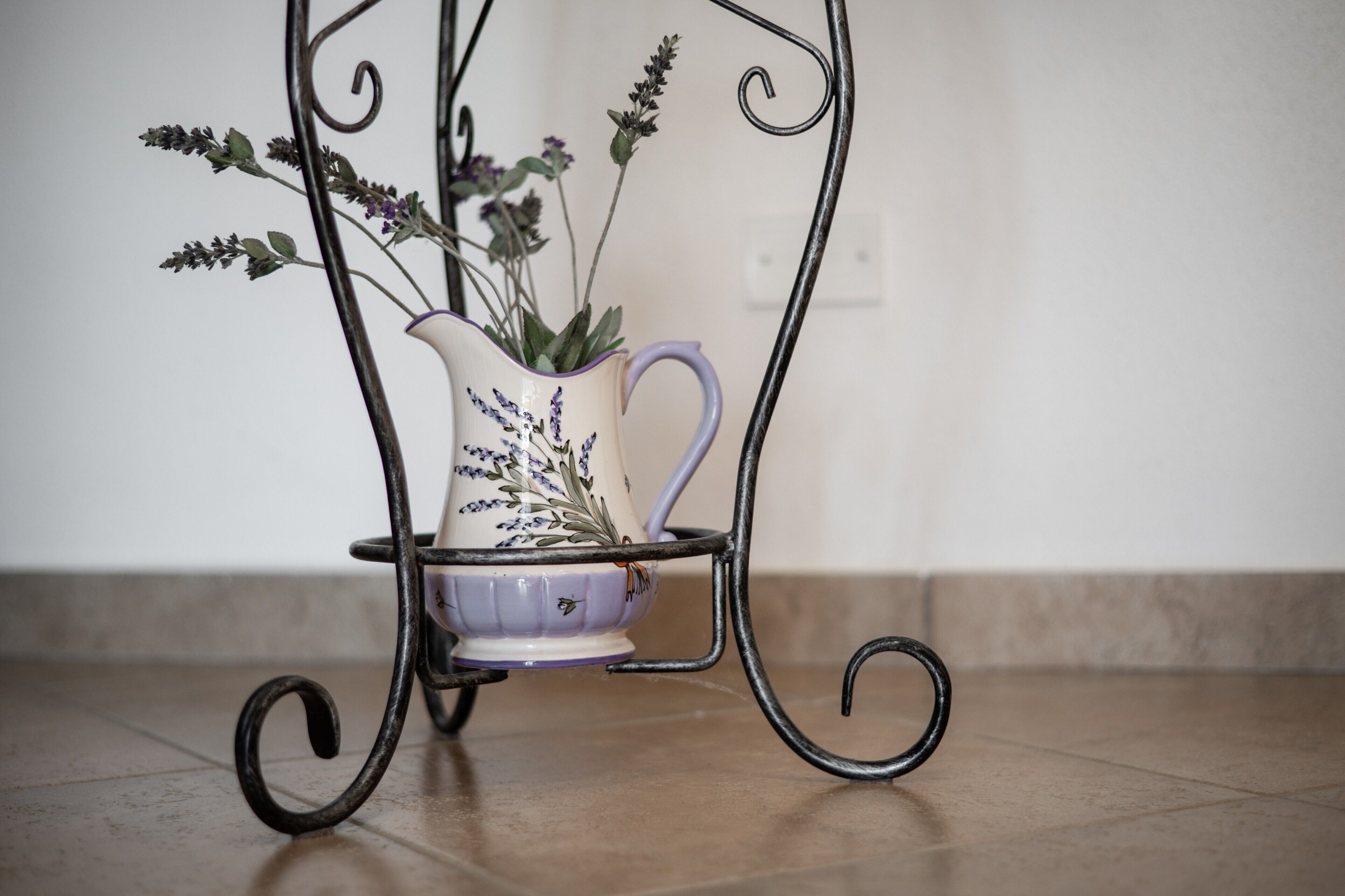 A metal stand with a white pitcher and a purple bowl containing lavender flowers.