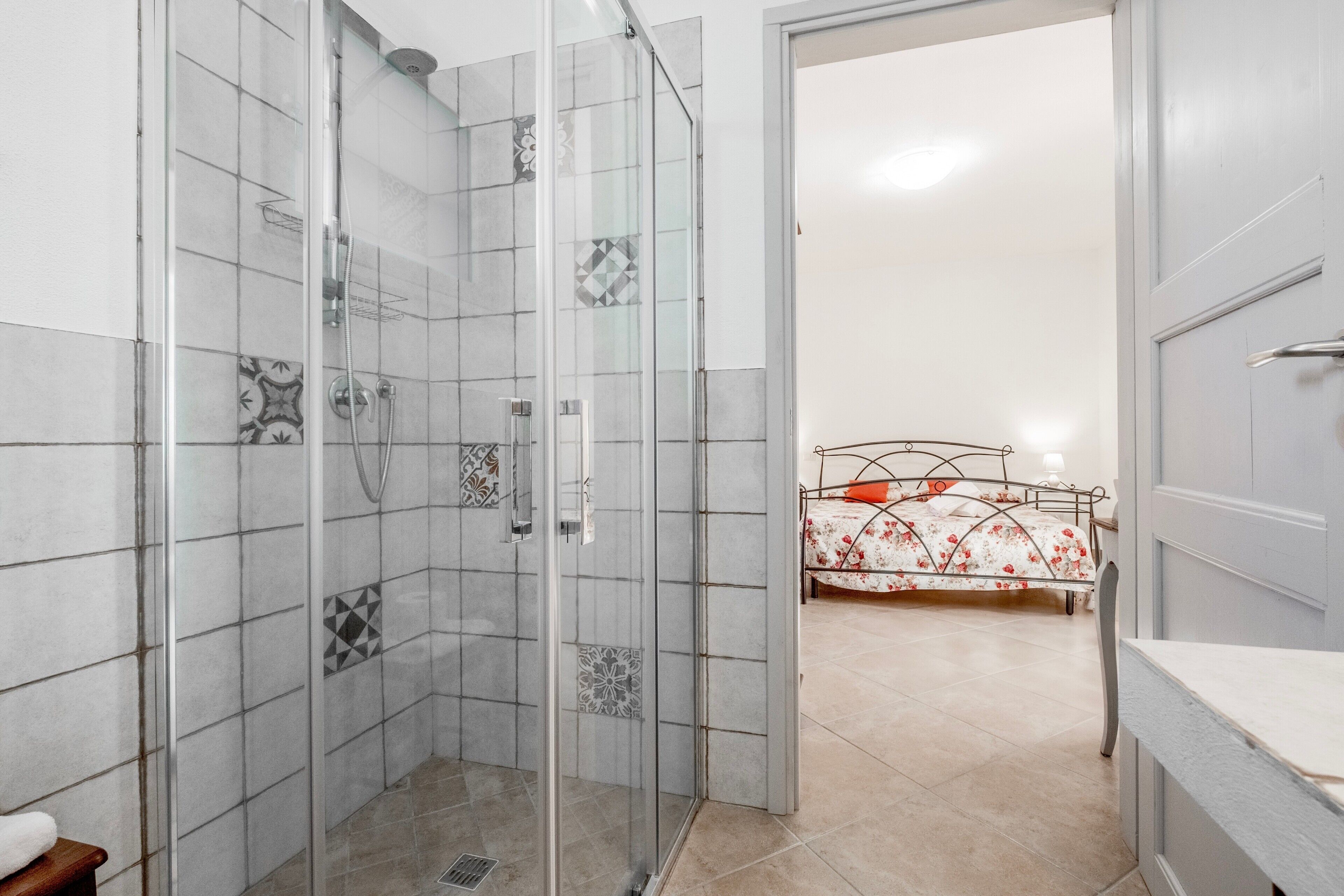 Een badkamer met een douche, een bed met bloemenprint beddengoed en een witte deur.