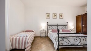 Quarto com duas camas de solteiro, um guarda-roupa de madeira e três ilustrações botânicas emolduradas na parede.