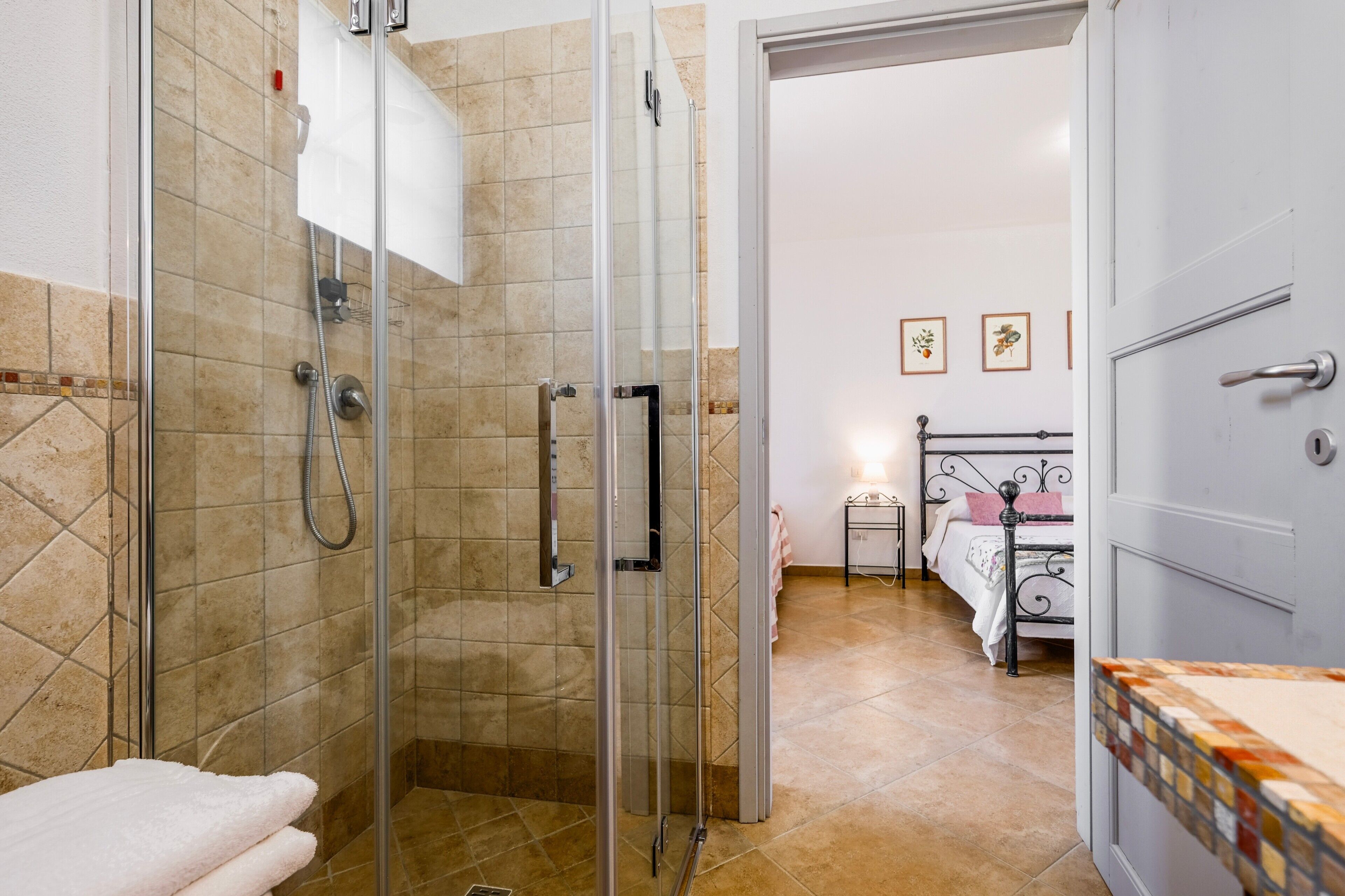 Ein Badezimmer mit einer Glaskabine zur Dusche, einem weißen Waschbecken und einem Bett mit Metallgestell.