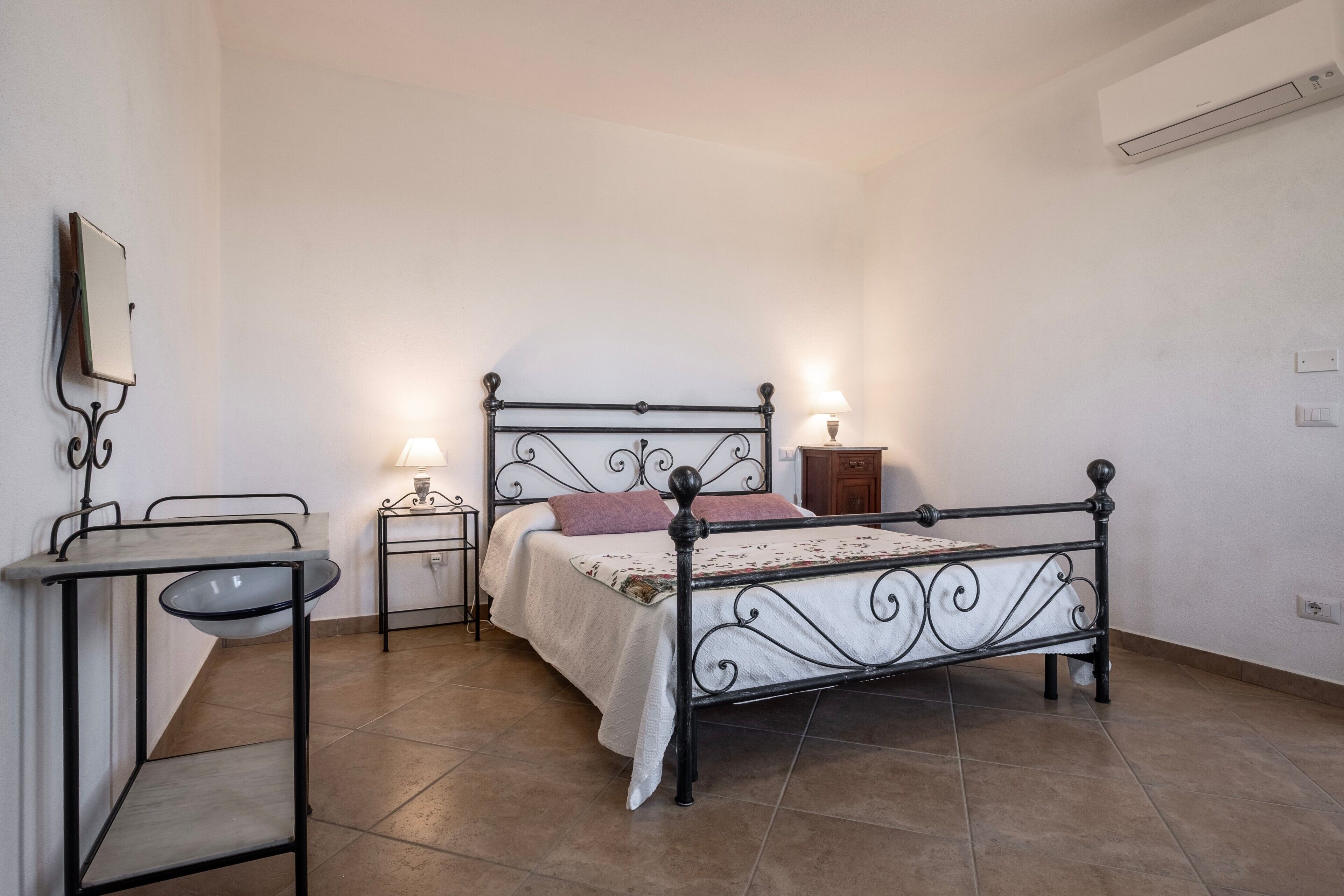Une chambre à coucher avec un lit en métal, une table de chevet, une lampe et un climatiseur fixé au mur.