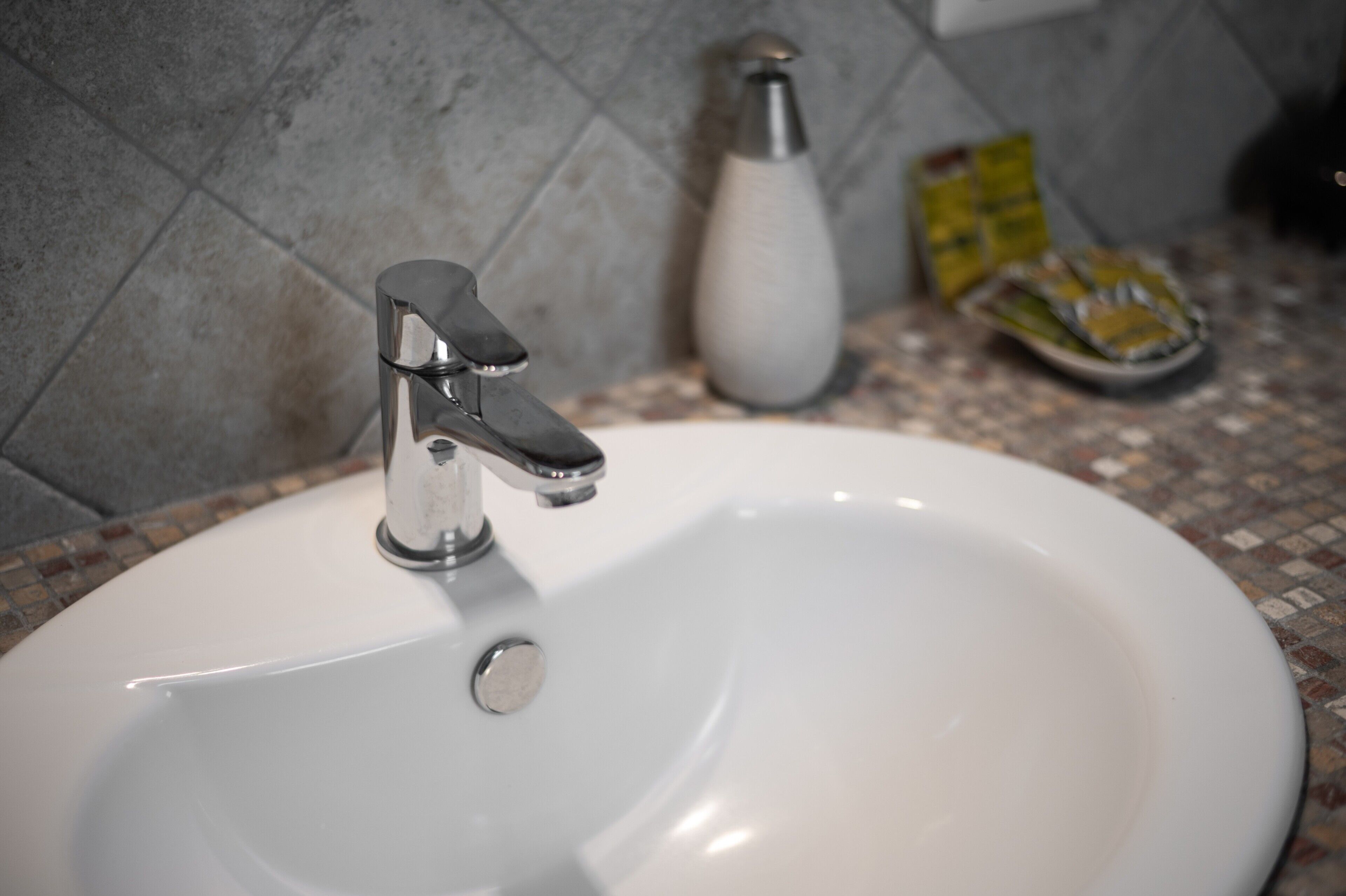 A bathroom sink with a chrome faucet, a white basin, and a tiled backsplash.