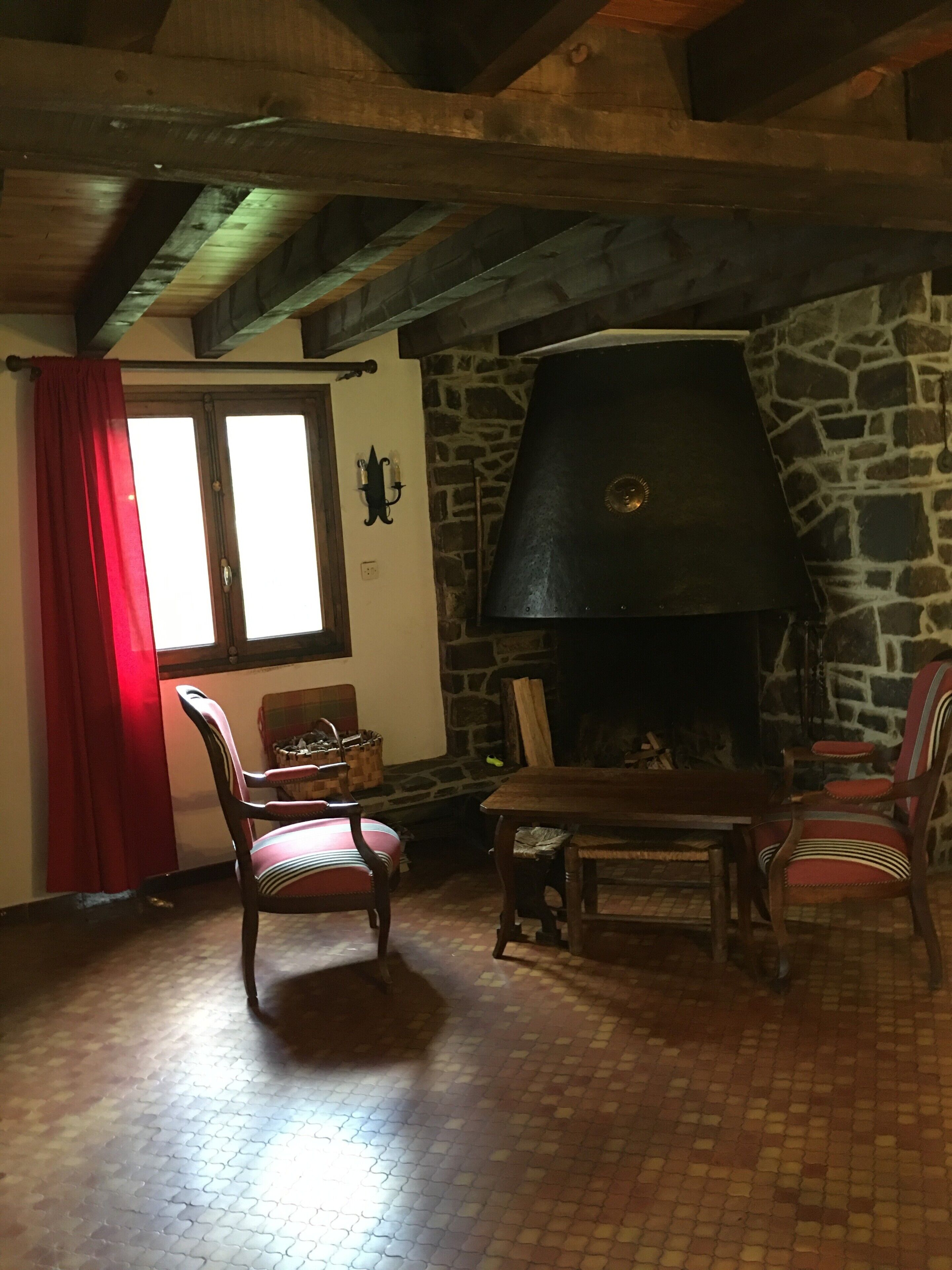 A rustic interior with a stone fireplace, wooden furniture, and a red curtain.