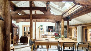 Un comedor rústico con una mesa y sillas de madera, una escalera con plantas y vistas a una cocina.