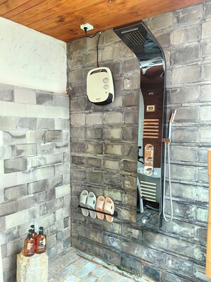 A stone-walled shower area with a built-in heater, a hose, and a shelf with slippers. - Jia Kedi Ancient House Cultural Homestay (Dali)