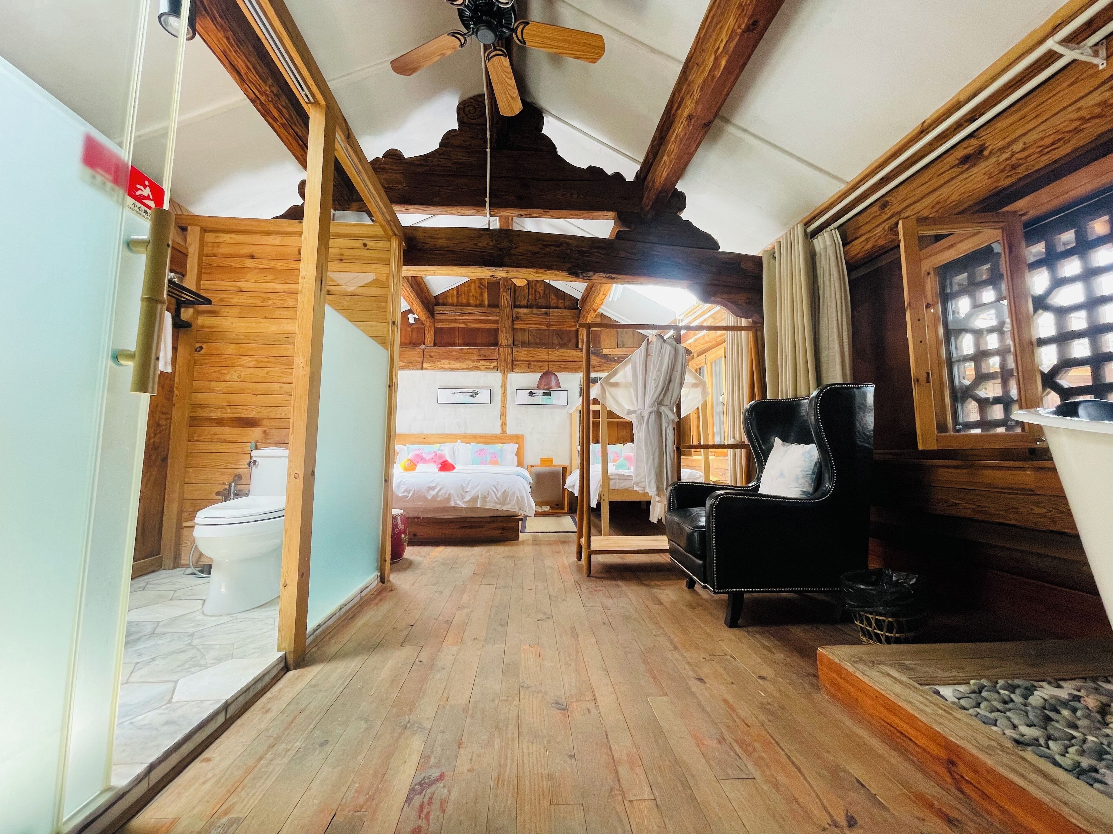 Een houten interieur met een bed, een zwarte lederen fauteuil, een houten plafond en een raam met een lattenwerkontwerp.