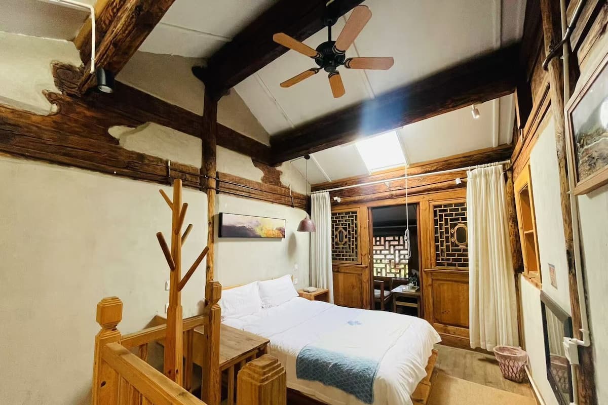 Ein Zimmer mit einem Holzbett, einem Deckenventilator und Blick auf ein traditionelles Gebäude durch ein Fenster.