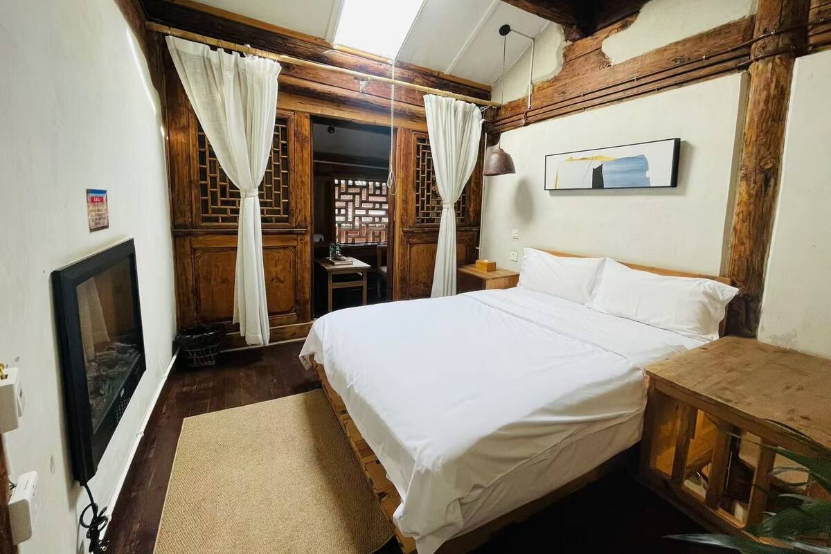 Ein Schlafzimmer mit einem Bett, einem Fernseher, Holzmöbeln und einem Fenster mit Vorhängen.