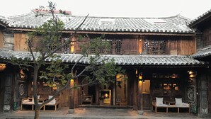 Un edificio tradicional de madera con tejado de baldosas, un patio con un estanque y zonas de estar.