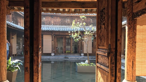 Un edificio tradicional de madera con un patio, piso de baldosas y un árbol.