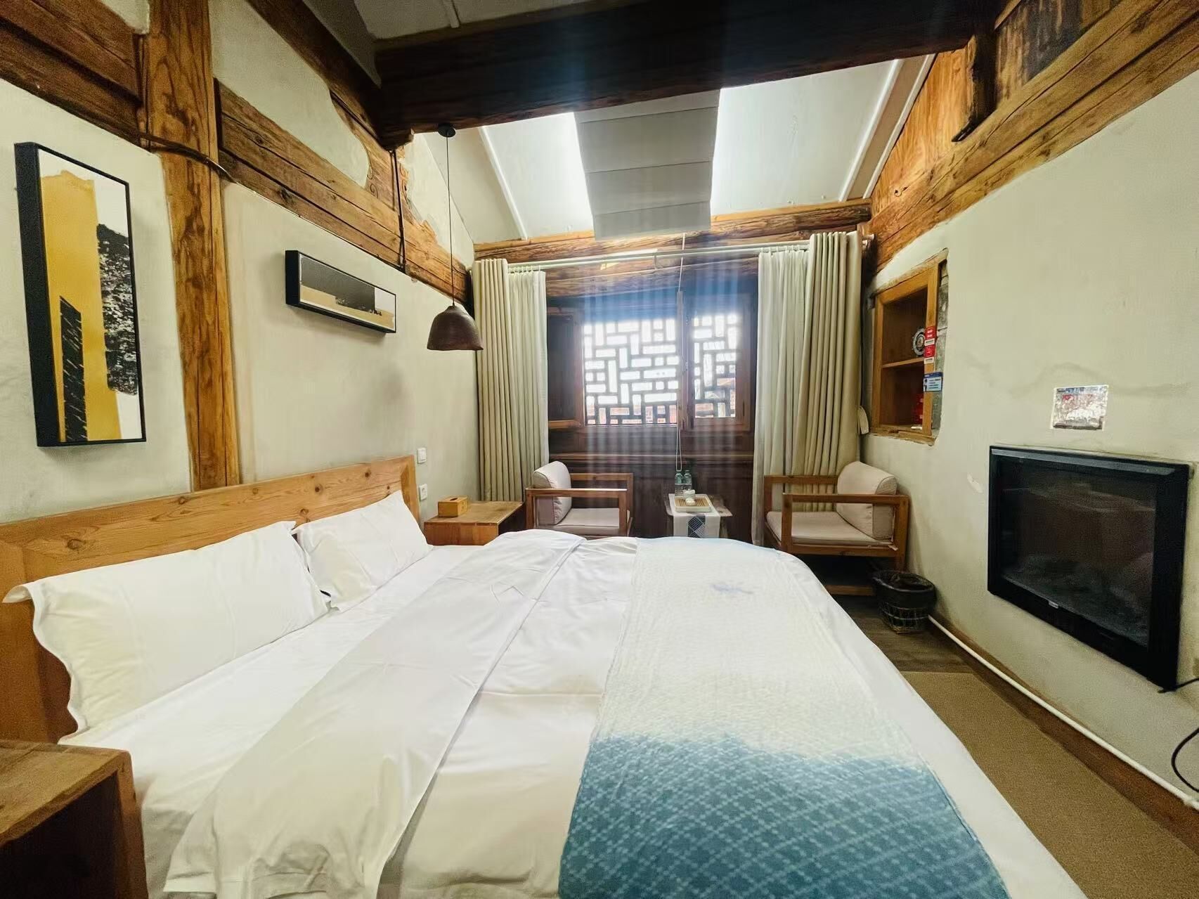 Une chambre d’hôtel avec un grand lit, des poutres apparentes, une télévision, une petite table et une chaise.