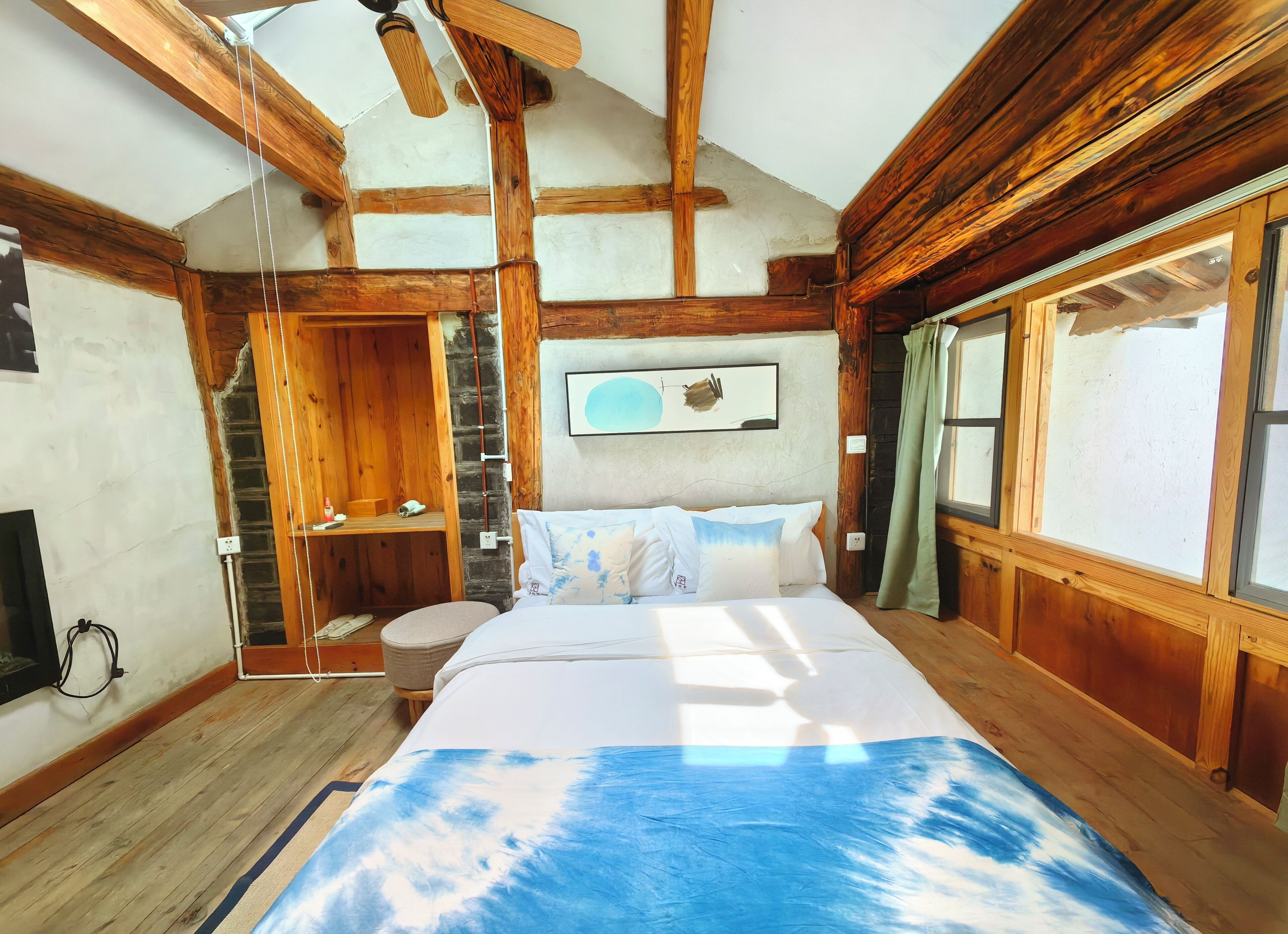 A wooden cabin bedroom with a bed, a wooden ladder, a window with curtains, and a ceiling fan.
