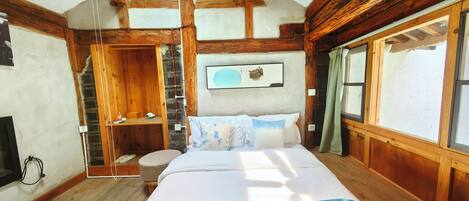A wooden cabin bedroom with a bed, a wooden ladder, a window with curtains, and a ceiling fan.