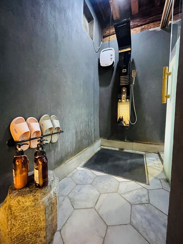 A bathroom with a shower, a towel rack with multiple towels, and two bottles on a stone pedestal.