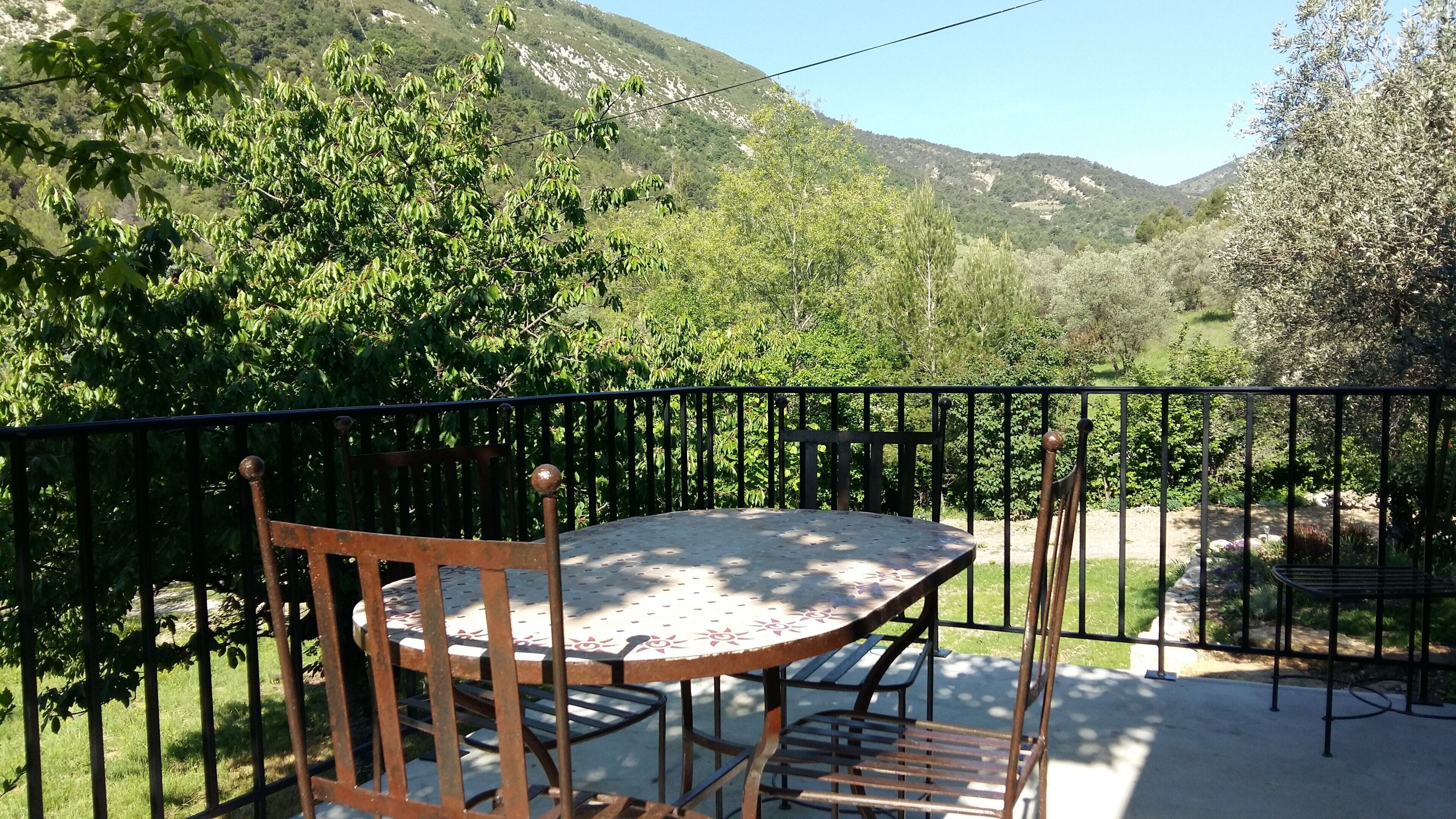 A balcony with a table and chairs, overlooking a mountainous landscape.