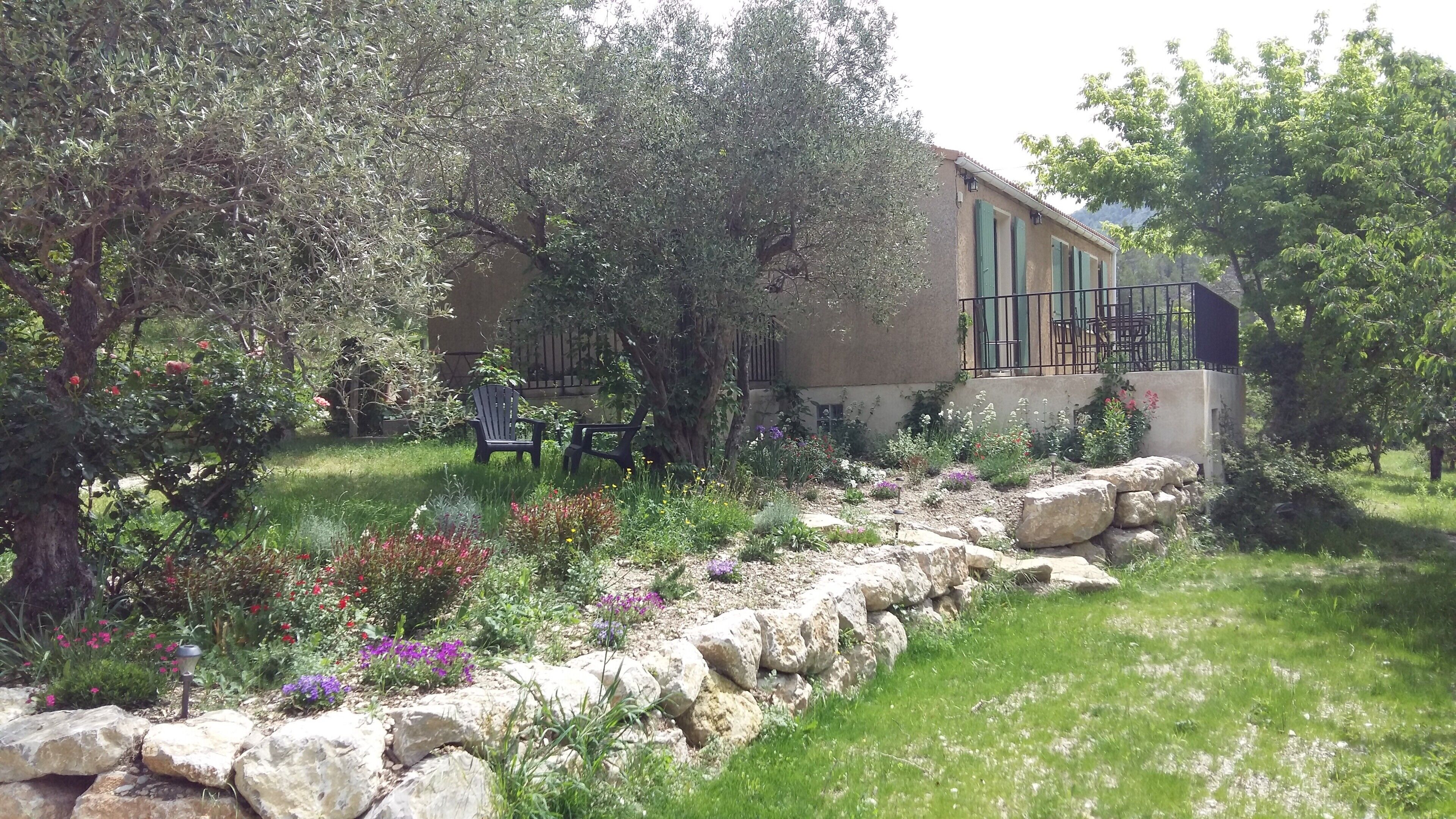 A building with a stone wall, outdoor seating, and a garden with various plants and flowers.