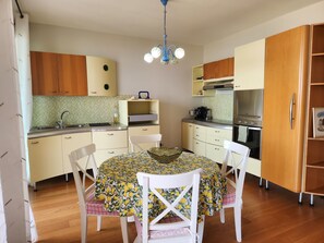 A compact kitchen with a dining table, chairs, a chandelier, and wooden cabinets.