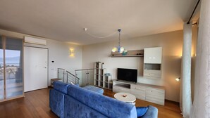 A modern living room with a blue sofa, a TV, and a staircase. - Apartment 'Alba Lake View   Pool' with Lake View, Shared Pool and Air Conditioning (Toscolano Maderno)