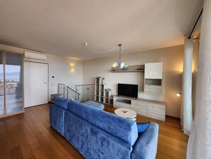 A modern living room with a blue sofa, a TV, and a staircase.