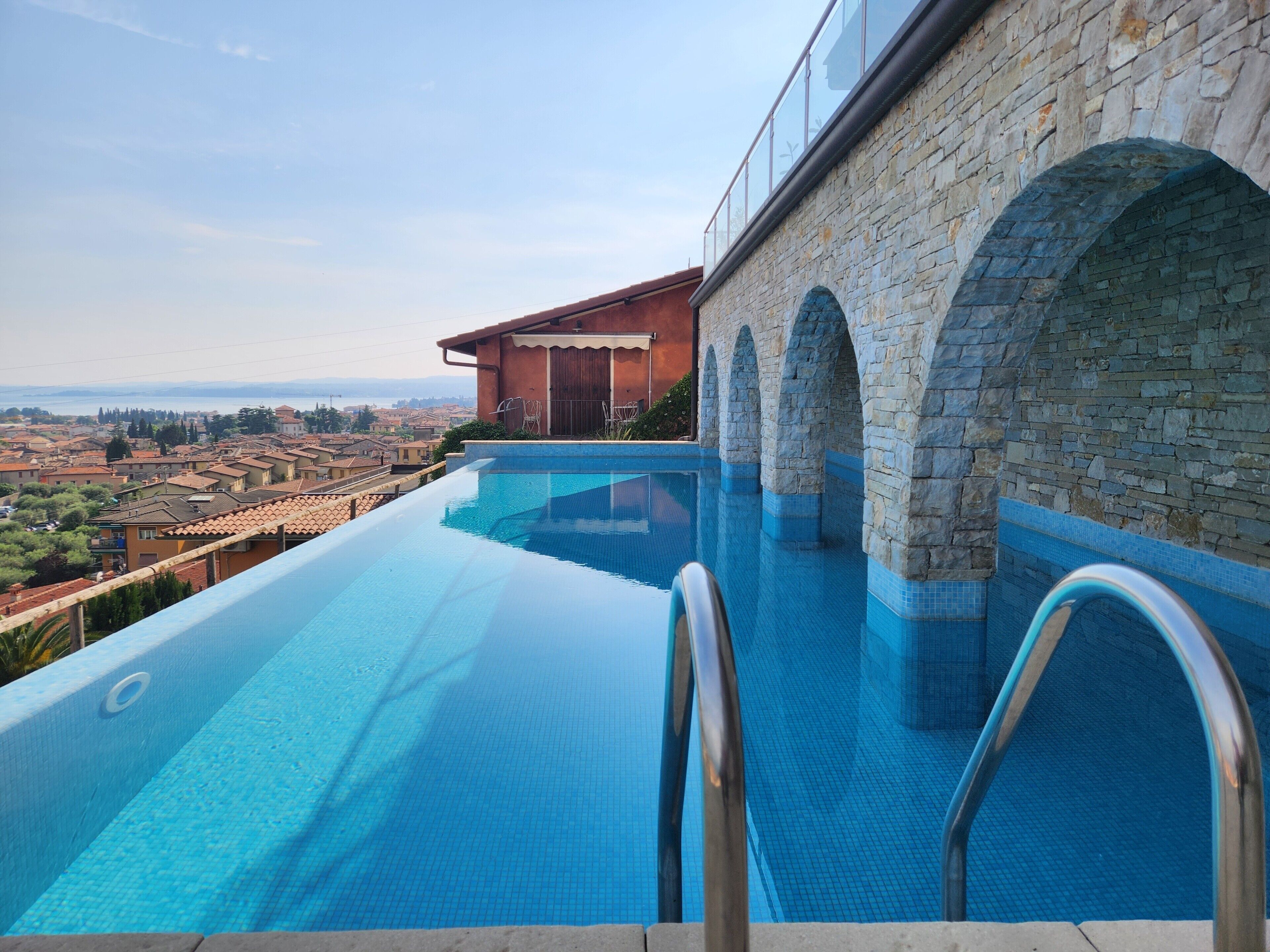 A swimming pool with stone arches, a clear view of the cityscape, and a modern building in the background.