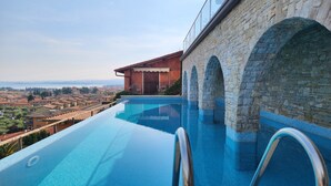 A swimming pool with stone arches, a clear view of the cityscape, and a modern building in the background. - Apartment 'Alba Lake View   Pool' with Lake View, Shared Pool and Air Conditioning (Toscolano Maderno)