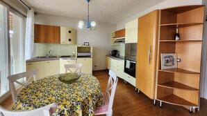 A compact kitchen with a dining table, chairs, a chandelier, and wooden cabinets. - Apartment 'Alba Lake View   Pool' with Lake View, Shared Pool and Air Conditioning (Toscolano Maderno)