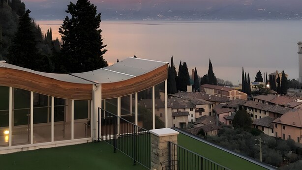 A modern building with a glass facade, a green roof, and a view of a lake and distant mountains. - Apartment 'Alba Lake View   Pool' with Lake View, Shared Pool and Air Conditioning (Toscolano Maderno)