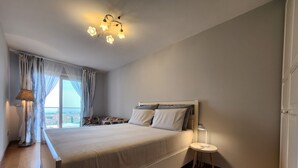 A bedroom with a large bed, a bedside table, a lamp, and a view through the window. - Apartment 'Alba Lake View   Pool' with Lake View, Shared Pool and Air Conditioning (Toscolano Maderno)