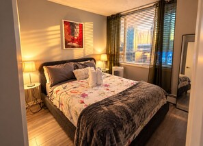 Une chambre d’hôtel avec un lit, deux lampes de chevet, une fenêtre avec des stores, un tableau au mur et un miroir.