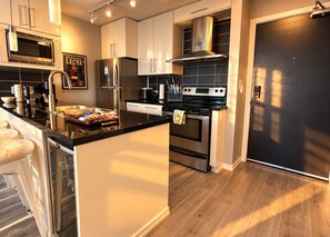 A modern kitchen with stainless steel appliances, a black countertop, and wooden flooring. - New 2025 Luxury Stadium views/Downtown Core (Vancouver)