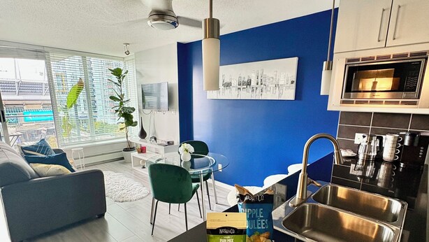 Eine moderne Küche mit schwarzem Arbeitsplatz, Spüle aus Edelstahl und einem Essbereich mit blauem Stuhl und weißem Tisch.