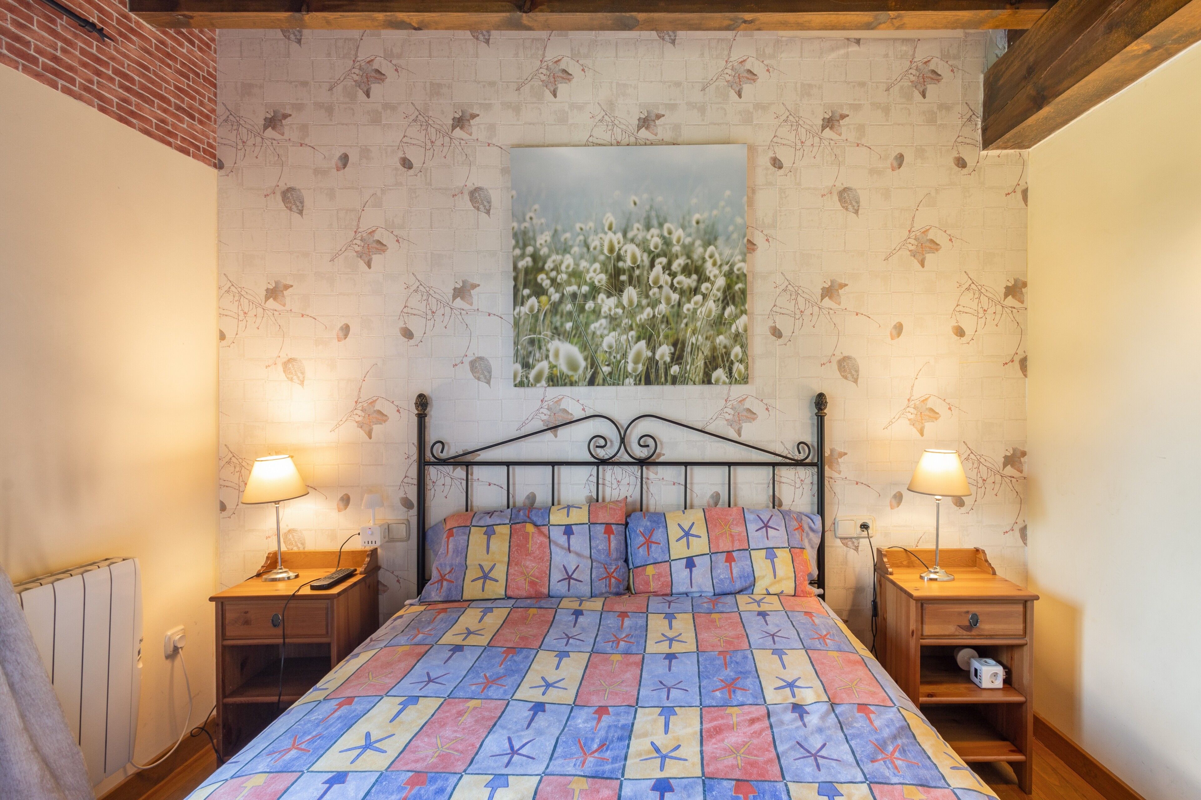 Un dormitorio con una cama, dos mesitas de noche, un cuadro en la pared y una pared de ladrillo.