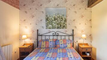 Un dormitorio con una cama, dos mesitas de noche, un cuadro en la pared y una pared de ladrillo.