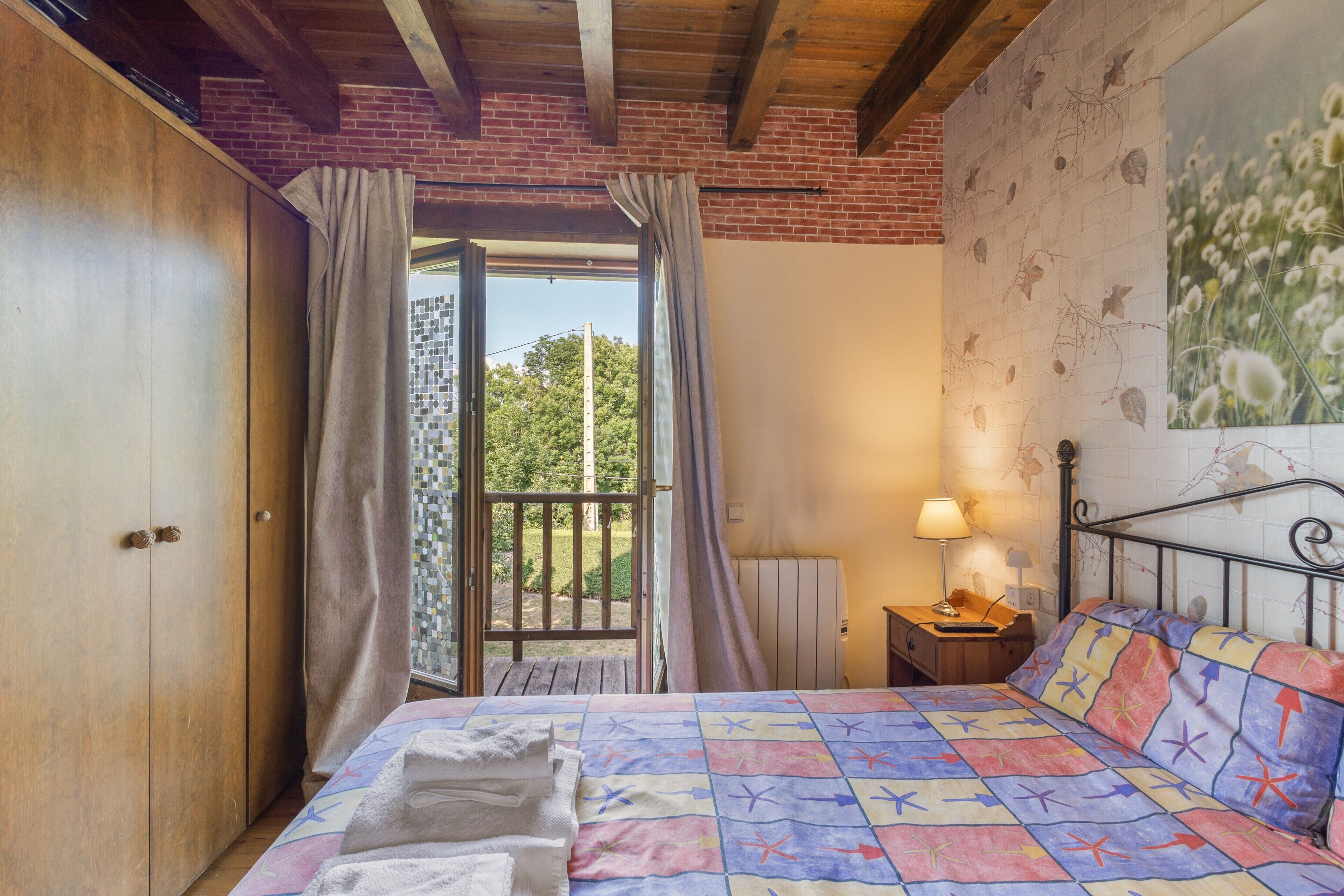 Une chambre à coucher avec un lit, une armoire en bois, une table de chevet avec une lampe, une fenêtre avec des rideaux et un mur en briques.