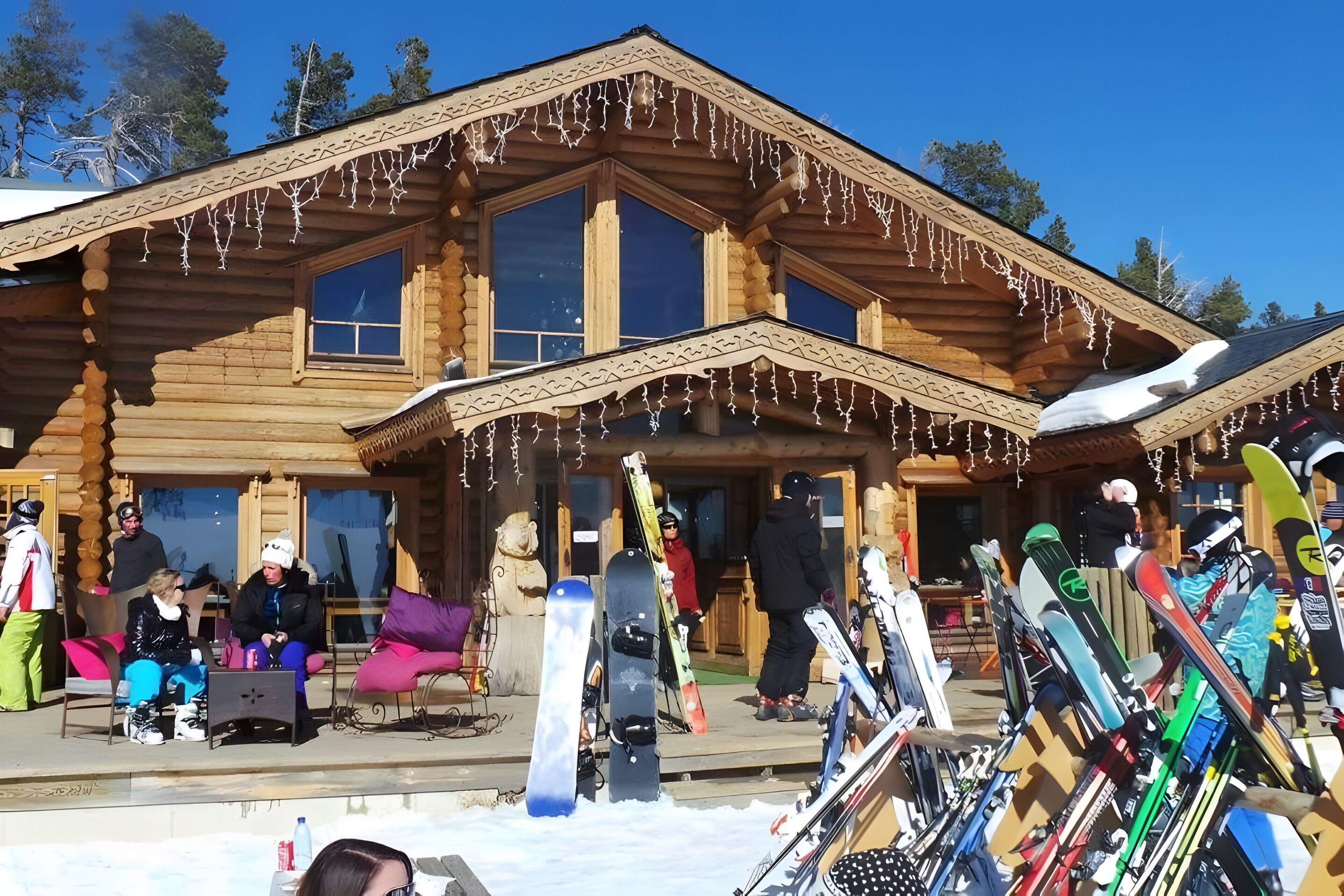 A wooden lodge with large windows, a porch, and snow-covered ground.