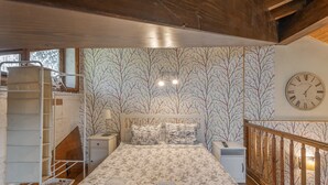 Een slaapkamer met een bed, nachtkastje, lamp, houten leuning en een wandklok.