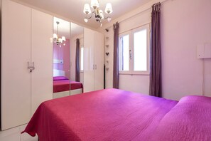A bedroom with a large bed, a wardrobe, a mirror, and a window with curtains.