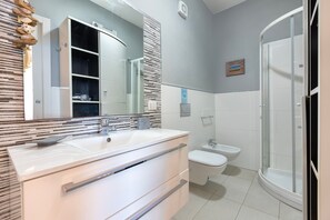 A modern bathroom with a large mirror, two sinks, a shower, and a toilet.